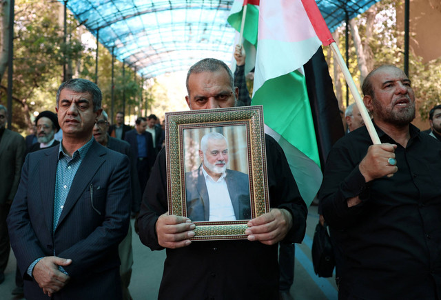 Orang-orang mengangkat bendera Palestina dan potret pemimpin Hamas yang terbunuh, Ismail Haniyeh, dalam sebuah unjuk rasa di Universitas Teheran, di ibu kota Iran, Teheran, pada 31 Juli 2024. Foto: AFP