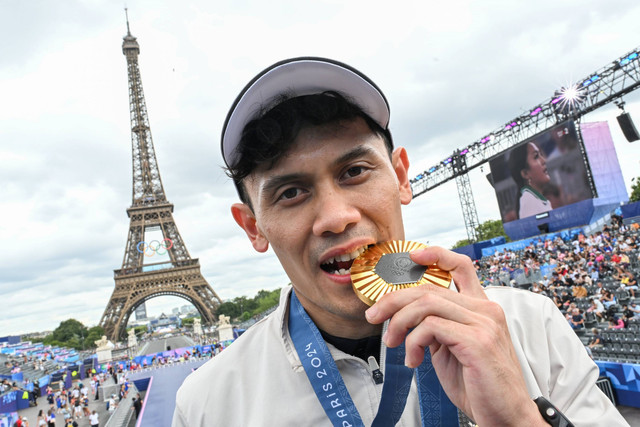 Atlet panjat tebing Indonesia Veddriq Leonardo menggigit medali emas dengan latar belakang Menara Eiffel di Champions Park, Trocadero, Paris, Prancis, Jumat (9/8/2024). Foto: Wahyu Putro A/ANTARA FOTO