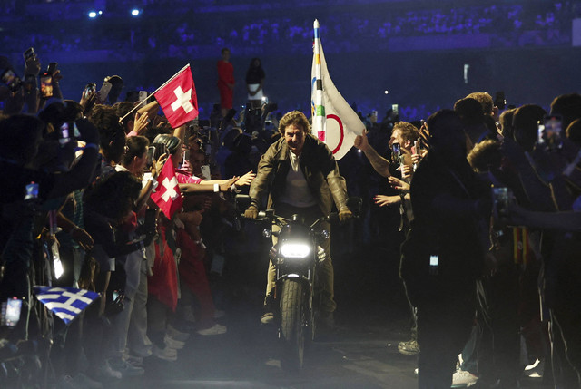 Aktor Tom Cruise mengendarai sepeda motor dengan bendera Olimpiade saat upacara penutupan Olimpiade Paris 2024 di Stade de France, Saint-Denis, Prancis, Minggu (11/8/2024). Foto: Gonzalo Fuentes/REUTERS