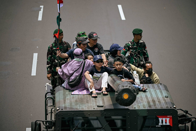 Sejumlah warga menaiki kendaraan tempur TNI saat konvoi dalam rangka menyambut HUT TNI ke-79 di Jalan Jenderal Sudirman, Jakarta, Sabtu (28/9/2024). Foto: Jamal Ramadhan/kumparan
