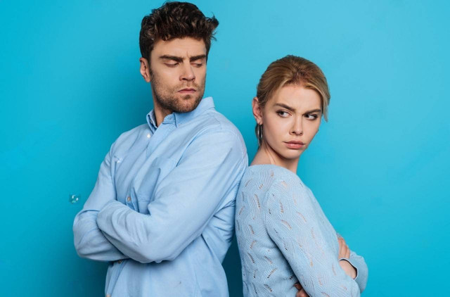 shutterstock : offended man and woman standing back to back with crossed arms on blue background