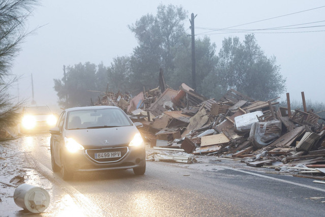 Mobil-mobil bergerak melewati barang-barang yang rusak dari sebuah pabrik mebel yang terkena dampak hujan lebat yang menyebabkan banjir di La Alcudia, wilayah Valencia, Spanyol, 30 Oktober 2024. Foto: Jon Nazca/Reuters