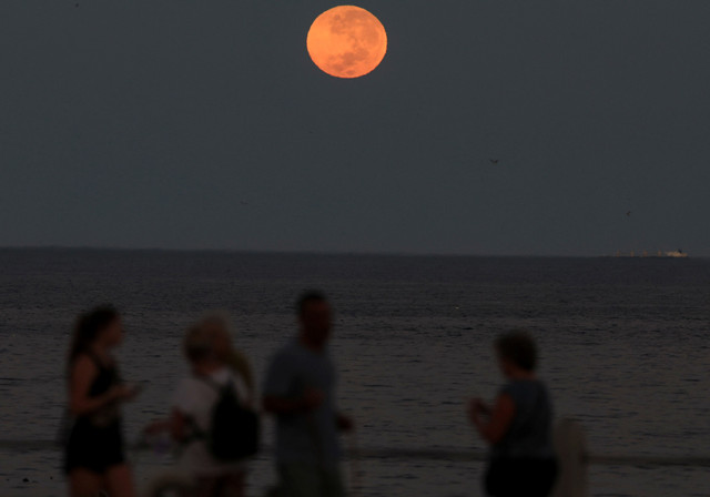 Bulan purnama terbenam selama gerhana bulan total, saat orang-orang berjalan di kawasan pejalan kaki Sea Point, di Cape Town, Afrika Selatan, 14 Maret 2025. Foto: REUTERS/Esa Alexander