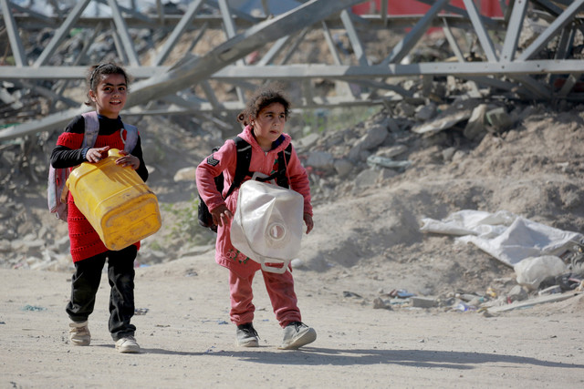 Dua anak Palestine membawa jeriken kosong dan barang-barang lainnya saat meninggalkan sektor timur Jalur Gaza setelah serangan udara Israel di Gaza, Selasa (18/3/2025). Foto: Bashar TALEB / AFP