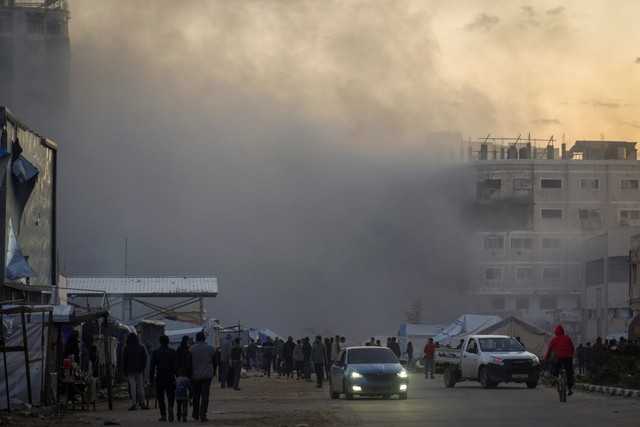 Warga melewati asap mengepul dari sebuah gedung setelah menjadi sasaran serangan tentara Israel di Kota Gaza, Sabtu (22/3/2025). Foto: Jehad Alshrafi/AP Photo