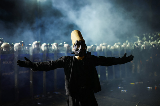 Seorang darwis berdiri di depan petugas polisi anti-huru-hara Turki selama unjuk rasa di Kota Istanbul, Minggu (23/3/2025). Foto: KEMAL ASLAN / AFP