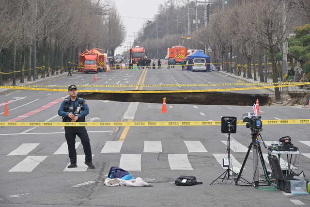 Polisi berjaga di dekat sinkhole di jalan Kota Seoul, Korea Selatan, Selasa (25/3/2025). Foto: ANTHONY WALLACE / AFP