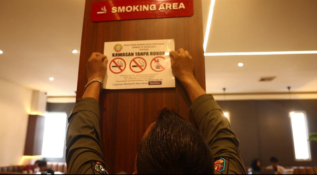 Petugas Pol PP Kota Pontianak saat menempelkan peringatan 'Kawasan Tanpa Rokok' di sebuah coffee shop di Pontianak. Foto; Dok. Istimewa