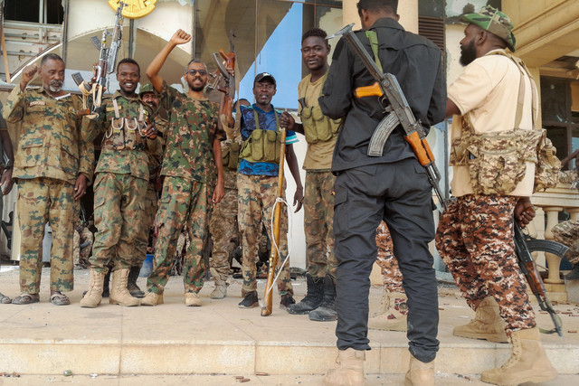 Tentara Sudan atau pasukan afiliasinya berpose untuk difoto sambil mengepalkan tangan di istana presiden yang rusak setelah merebut kembali kompleks tersebut dari paramiliter RSF di Khartoum pada 21 Maret 2025. Foto: AFP