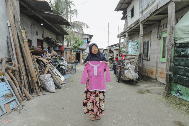 Penerima Baju: Anak penerima program kumparan 'Cerita Baru untuk Bajumu' menunjukkan baju yang diterimanya di Kampung Pemulung, Duren Sawit, Jakarta Timur. Foto: Jamal Ramadhan/kumparan