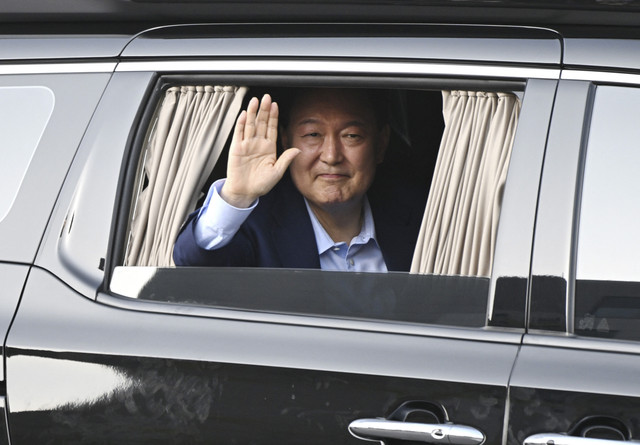 Mantan Presiden Korea Selatan Yoon Suk-yeol melambaikan tangan dari kendaraanya saat melintas keluar rumah dinas di Seoul, Korea Selatan, Jumat (11/4/2025). Foto: Jung Yeon-je/AFP