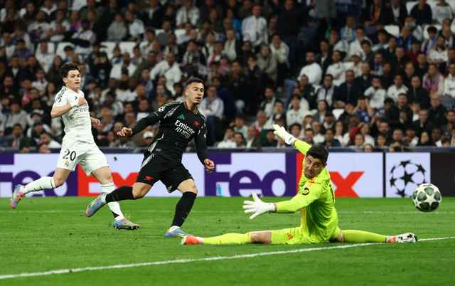 Gabriel Martinelli (tengah) bobol gawang Thibaut Courtois (kanan) saat laga Real Madrid vs Arsenal dalam leg kedua perempat final Liga Champions 2024/25 di Estadio Santiago Bernabeu pada Kamis (17/4) dini hari WIB. Foto: Action Images via Reuters/Lee Smith