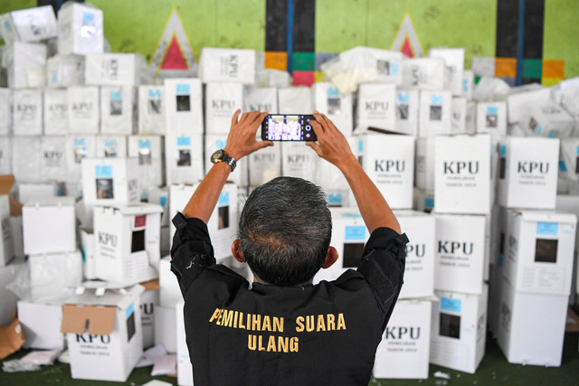 Petugas Bawaslu memotret logistik pemungutan suara ulang (PSU) dengan telepon genggamnya di gudang logistik KPU Kutai Kartanegara di Tenggarong, Kukar, Kalimantan Timur, Kamis (17/4/2025). Foto: M Risyal Hidayat/ANTARA FOTO