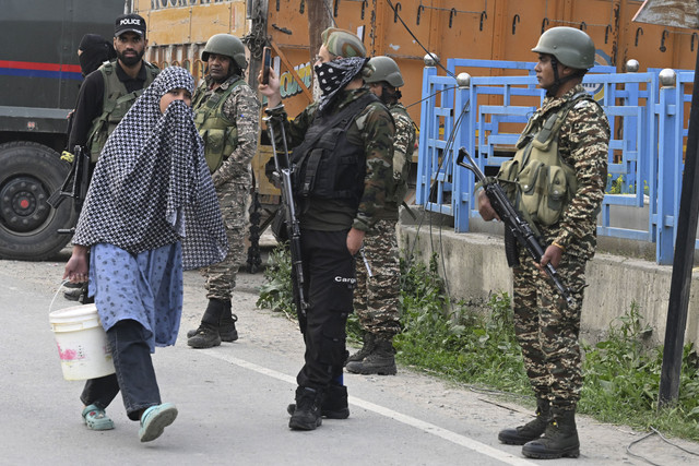 Personel keamanan India berjaga saat seorang wanita berjalan di sepanjang jalan di Wuyan dekat kota utama Srinagar di Kashmir yang dikelola India, Rabu (7/5/2025). Foto: TAUSEEF MUSTAFA/AFP