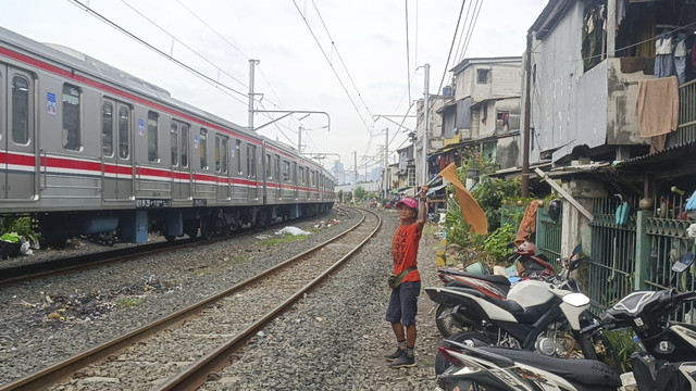 Potret Dani (57), warga sekitar perlintasan sebidang Roxy yang pegang peran vital untuk memperingati pemotor yang menyeberangi rel akan kedatangan kereta dengan bendera oranyenya, Jumat (23/5/2025). Foto: Thomas Bosco/kumparan