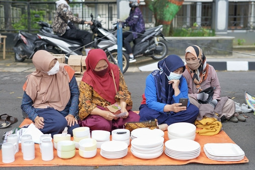 Perempuan pedagang sedang menjajakan barang jualan dan tengah menggunakan gadget [Tim Dokumentasi MicroSave Consulting/2024]
