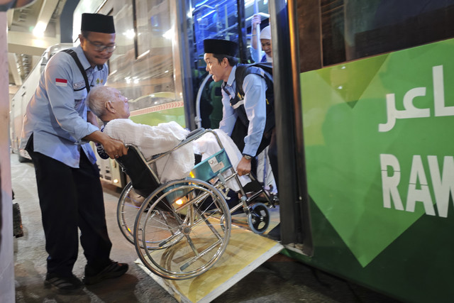 Petugas layanan lansia PPIH Arab Saudi Abdurrahman (kiri) dan rekannya menurunkan kursi roda yang dinaiki calon haji lansia Soemarno, sesampainya di terminal Jabal Kakbah yang berada di dekat Masjidil Haram. Foto: Andika Wahyu/ANTARA FOTO