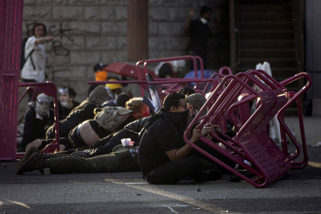 Para demonstran berlindung di balik barikade darurat ketika bentrokan dengan aparat keamanan saat melakukan aksi protes menentang razia imigrasi federal di pusat kota Los Angeles, California, Minggu (8/6/2025). Foto: ETIENNE LAURENT/AFP