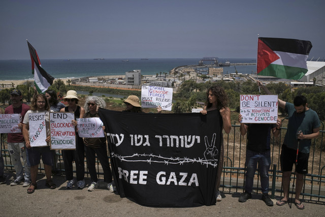 Orang-orang melambaikan bendera Palestina dan memegang tanda untuk mendukung Greta Thunberg dan aktivis lainnya yang mencoba mengirimkan bantuan ke Gaza di dekat pelabuhan Ashdod, Israel, Senin (9/6/2025). Foto: Leo Correa/AP Photo