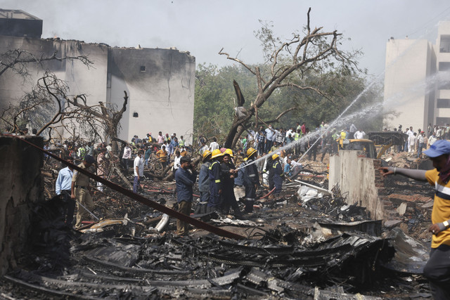 Orang-orang berkumpul di dekat bangunan yang rusak dan pepohonan saat petugas pemadam kebakaran bekerja di lokasi jatuhnya pesawat Air India di Ahmedabad, India, Kamis (12/6/2025). Foto: Amit Dave/REUTERS