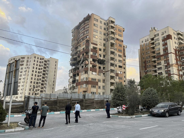 Warga menyaksikan sebuah apartemen yang rusak di Teheran, Iran, Jumat (13/6/2025). Foto: Vahid Salemi/AP Photo