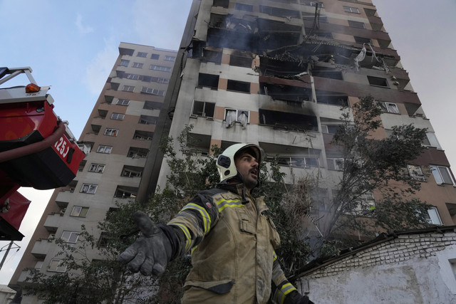 Seorang petugas pemadam kebakaran memanggil rekan-rekannya di lokasi ledakan di sebuah kompleks perumahan di Teheran utara, Iran, Jumat (13/6/2025). Foto: Vahid Salemi/AP Photo