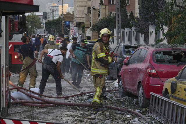 Petugas pemadam kebakaran dan warga membersihkan lokasi ledakan di sebuah kompleks perumahan setelah serangan Israel di Teheran, Jumat (13/6/2025). Foto: Vahid Salemi/AP Photo