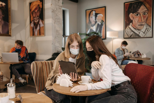 Ilustrasi mahasiswa mengerjakan tugas (sumber: https://www.pexels.com/video/young-women-with-face-masks-using-tablet-in-coffee-shop-6024569/)
