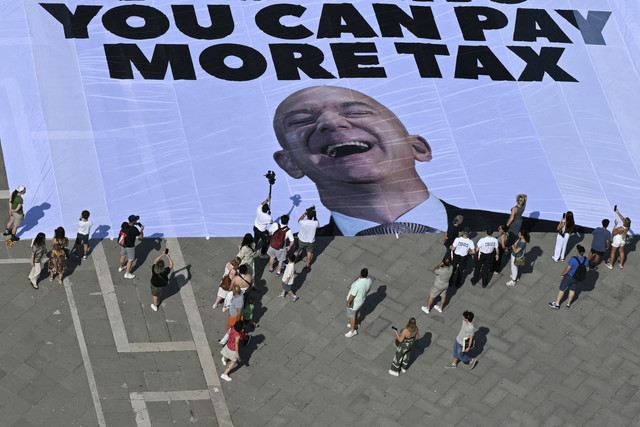 Sejumlah aktivis kelompok lingkungan internasional Greenpeace membentangkan spanduk raksasa yang menampilkan foto Jeff Bezos menjelang pernikahan Jeff Bezos di alun-alun St Mark, Venesia, Senin (23/6/2025). Foto: Stefano Rellandini/AFP