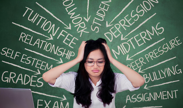 Gambar ini menunjukkan seorang wanita muda yang stres, memegangi kepalanya di depan papan tulis yang penuh dengan tulisan berbagai tekanan akademik dan personal seperti biaya kuliah, tugas, depresi, ujian, hingga *peer pressure* dan *bullying*. Sumber: https://id.pinterest.com/