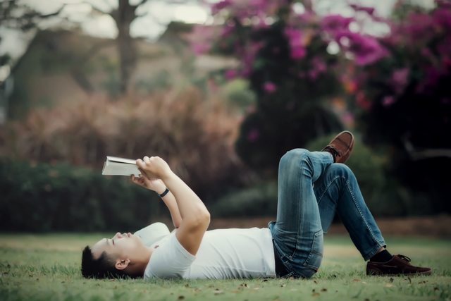 Pemuda dengan tenang sambil membaca buku ditaman, dikeliling keramaian orang-orang yang berjalan cepat di latar belakang. Foto: freepik.com