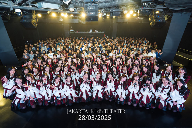 Gambar tersebut menunjukkan grup idola JKT48 yang sedang berpose di atas panggung di hadapan penonton yang memenuhi sebuah teater. Para anggota JKT48 mengenakan seragam panggung berwarna putih, merah, dan hitam. Di bagian bawah gambar terdapat teks "JAKARTA JKT48 THEATER" dan tanggal "28/03/2025". Sumber: https://x.com/officialJKT48