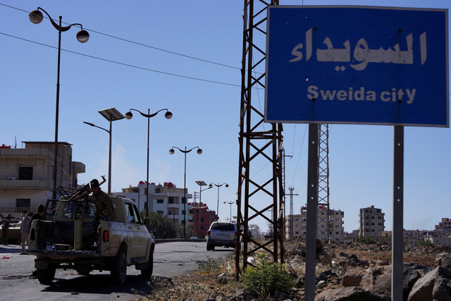 Pasukan keamanan Suriah berkumpul di dekat rambu jalan bertuliskan 'Kota Sweida' setelah bentrokan selama dua hari di Sweida, Suriah, Selasa (15/7/2025). Foto: Karam al-Masri/ REUTERS