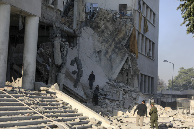 Dua warga melihat bangunan yang hancur akibat serangan Israel ke markas besar militer dan kementerian pertahanan Suriah di Damaskus, Suriah, Rabu (16/7/2025). Foto: Bakr Alkasem/AFP