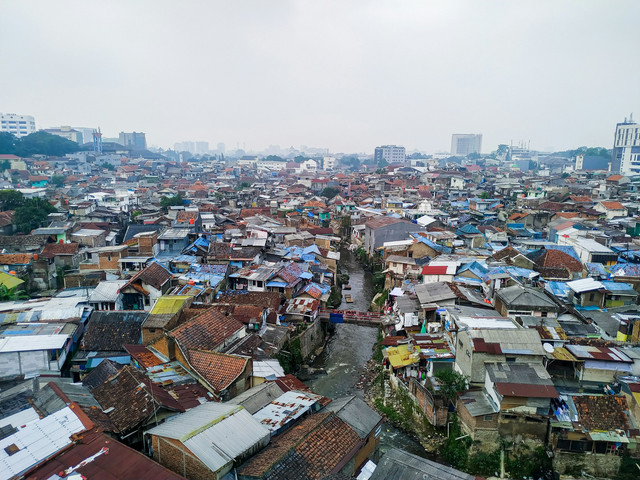 Permukiman padat penduduk di kawasan perkotaan dengan rumah-rumah berdempetan dan saluran air di tengah, mencerminkan ketimpangan infrastruktur dan kondisi kemiskinan di kota besar Indonesia. Foto oleh Bagas Harfianto di Unsplash