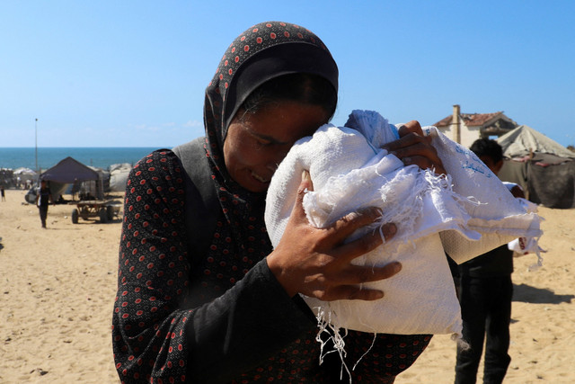 Seorang ibu Palestina yang mengungsi, Zainab Dakka memegang sekantong tepung yang dibawanya dari pengiriman bantuan yang memasuki Gaza melalui Israel di Kota Gaza, Jumat (1/8/2025). Foto: Ebrahim Hajjaj/REUTERS