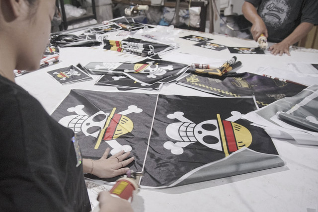 Pekerja memotong bendera yang menggambarkan Jolly Roger dari serial anime dan manga Jepang populer 'One Piece' di toko penjual bendera khusus di Karanganyar, Jawa Tengah, Kamis (7/8/2025). Foto: Budi Purwanto/Reuters