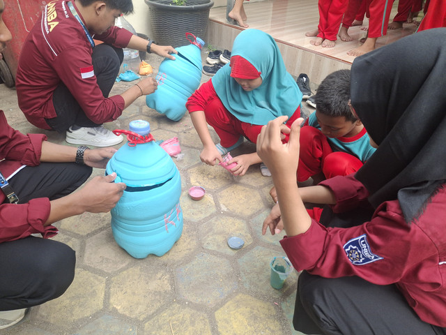 Siswa SDN Wilulang mengecat galon bekas yang disulap menjadi tempat sampah, didampingi mahasiswa KKM 18 UNIBA