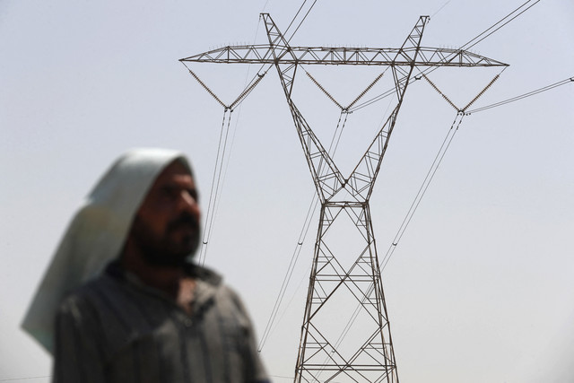 Seorang pria Irak berdiri di bawah menara transmisi listrik di tengah suhu yang terus meningkat, kekurangan air kronis, dan pemadaman listrik di Kota Hilla, Irak, Minggu (10/8/2025). Foto: Ahmad Al-Rubaye/AFP