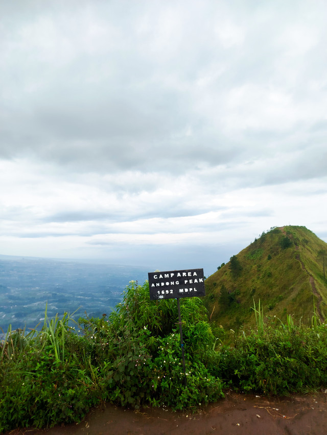 Foto Area Berkemah Gunung Andong di Magelang, dengan papan penanda Camp Area 1692 mdpl, menampilkan jalur hijau dan panorama luas yang menawan.