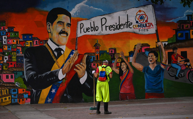 Seorang petugas  membersihkan area di depan mural yang menggambarkan Presiden Venezuela Nicolas Maduro di Caracas, (27/8/2025). Foto: Juan Barreto/AFP