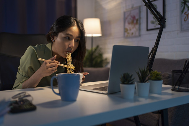 Ilustrasi wanita makan mie sambil screen time. Foto: PBXStudio/Shutterstock
