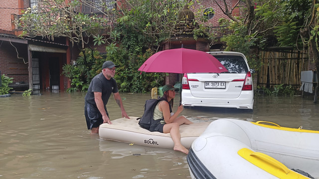 Derk (laki-laki, 50 tahun), wisatawan asal Afrika Selatan tampak menikmati momen mendorong istrinya yang duduk santai di matras angin di tengah banjir di Jalan Dewi Saraswati III, Kelurahan Seminyak, Kabupaten Badung, Bali, Rabu (10/9/2025) Foto: Denita BR Matondang/kumparan