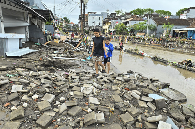 Warga berjalan di jalanan yang rusak akibat diterjang banjir di kawasan Jalan Bukit Barisan, Denpasar, Bali, Rabu (10/9/2025). Foto: Fikri Yusuf/ANTARA FOTO