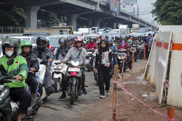 Seorang pekerja berjalan di dekat pengendara sepeda motor saat pelaksanaan rekayasa lalu lintas di Gerbang Tol (GT) Fatmawati 2 kawasan Jalan TB Simatupang, Jakarta, Selasa (16/9/2025). Foto: Iqbal Firdaus/kumparan