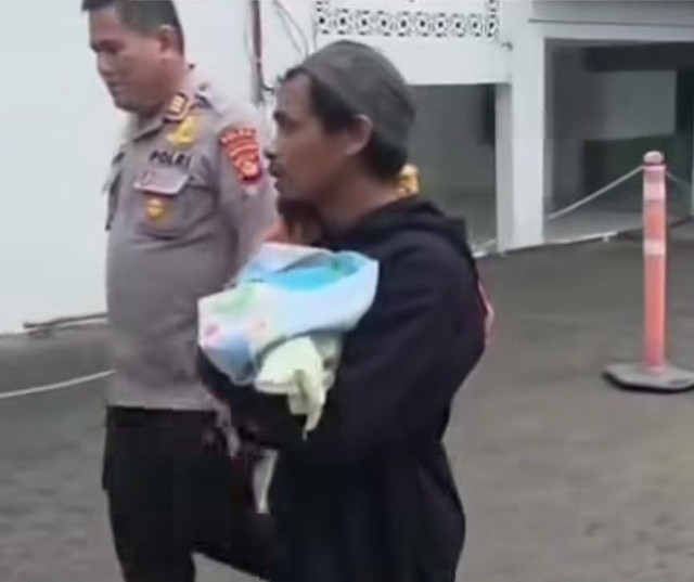 Saat Joko menggendong jenazah bayinya yang ditemani anggota polisi Polsek Kertapati, Palembang. Foto : Istimewa