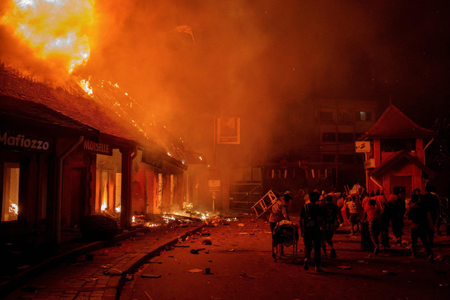 Para pekerja menyelamatkan barang-barang mereka dari toko-toko yang terbakar selama demonstrasi untuk mengecam pemadaman listrik dan kekurangan air yang sering terjadi di Antananarivo, Madagaskar, Kamis (25/9/2025). Foto: Zo Andrianjafy/Reuters