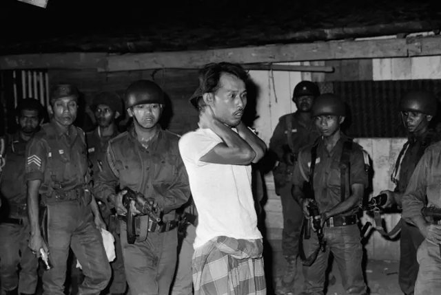 Seorang terduga simpatisan G30S dipriksa di bawah todongan senjata. Foto: Bettmann/Getty Images.