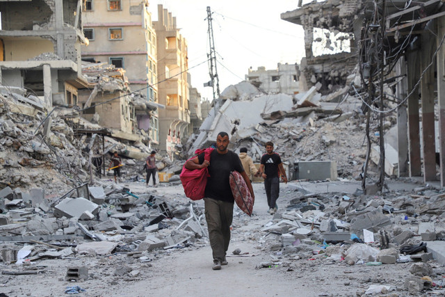 Warga berjalan di tengah kehancuran di Kota Gaza, Jalur Gaza utara, Minggu (12/10/2025). Foto: Ebrahim Hajjaj/REUTERS