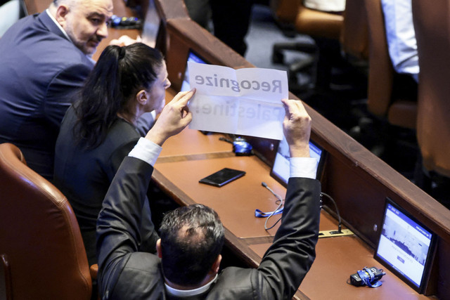 Seorang anggota parlemen Israel memegang plakat bertuliskan: 'Akui Palestina!' di Knesset pada hari pidato Presiden AS Donald Trump di Yerusalem, Senin (13/10/2025). Foto: Evelyn Hockstein/REUTERS